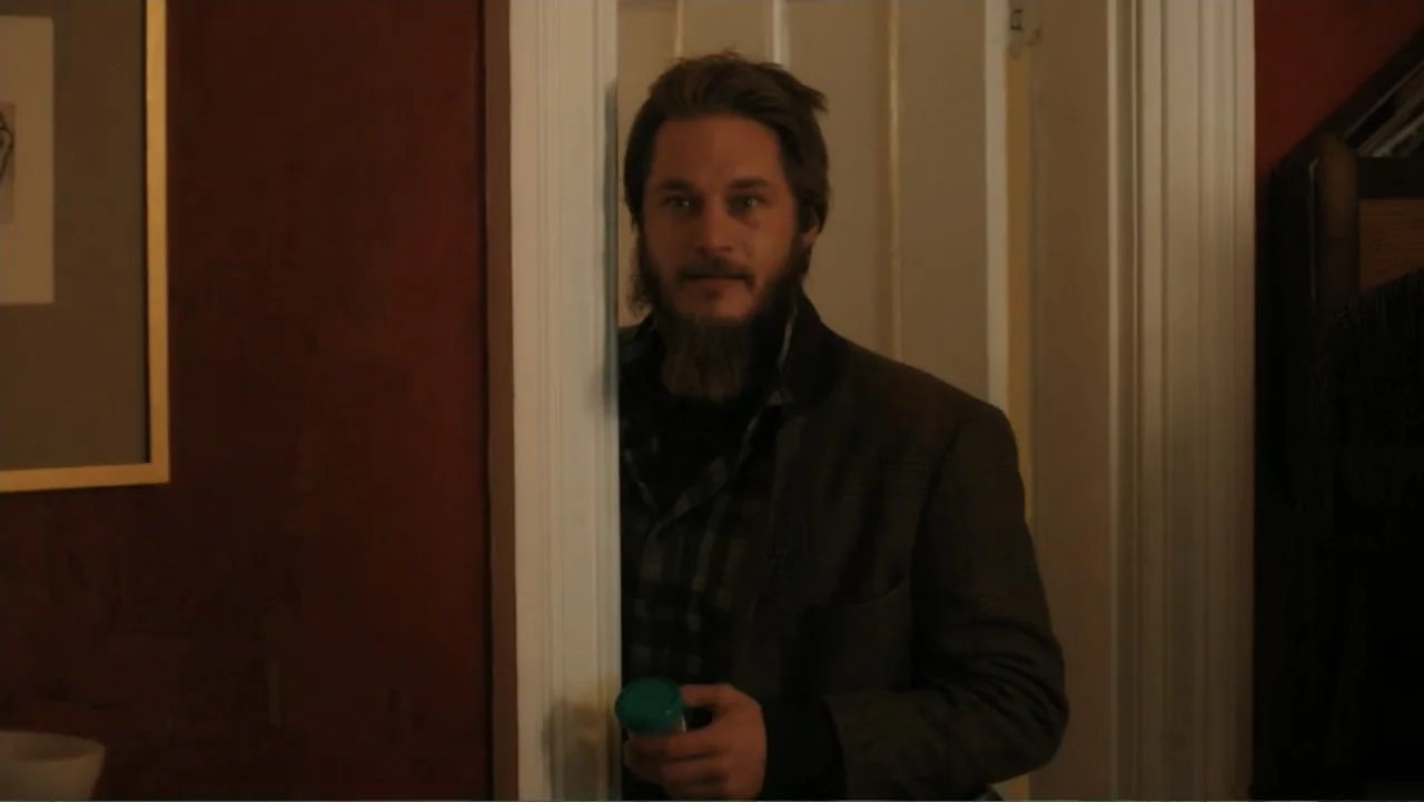 Maggie's Plan (2016) movie still: medium — A dimly lit room features dark red walls and white door frame trim. A bearded man stands in the open…