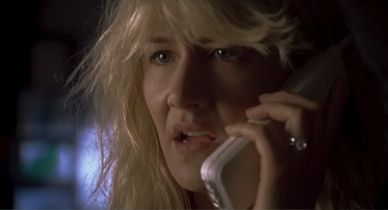 Jurassic Park III (2001) movie still: closeup — An interior space features a woman in low light during the nighttime. A blonde woman holds a white…