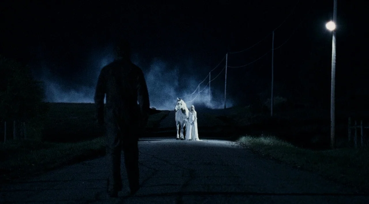 Halloween 2 (2009) movie still: wide — A dark rural road stretches through a landscape marked by telephone poles and night mist. A man in dark…