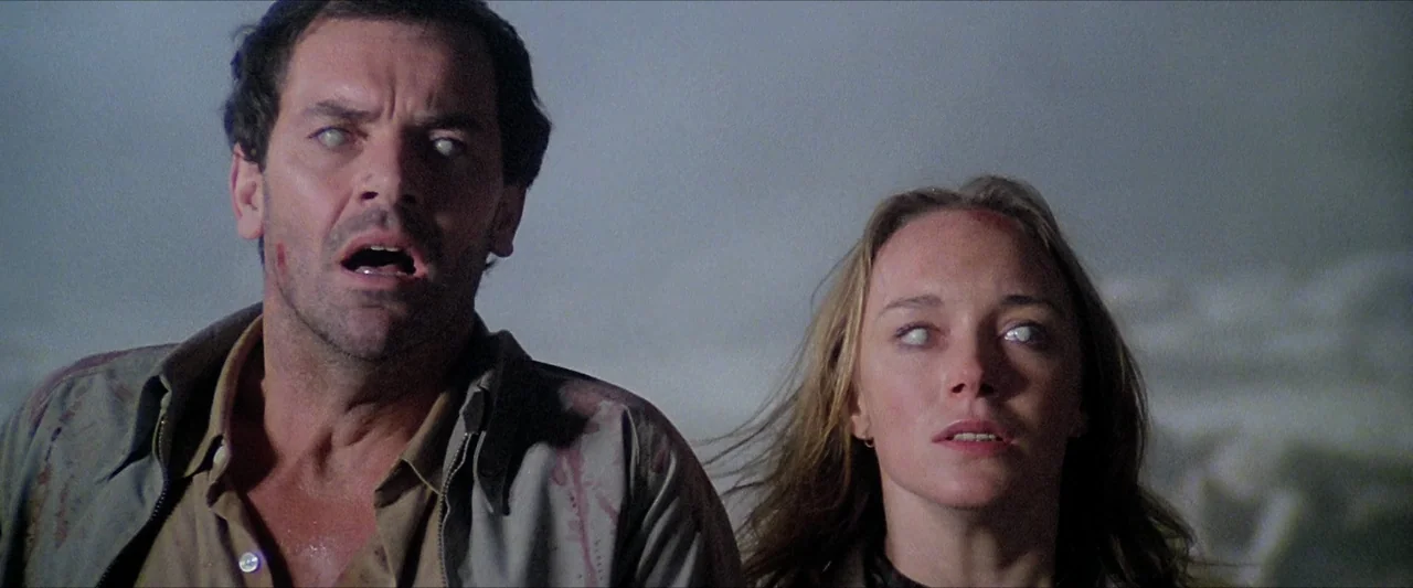 The Beyond (1981) movie still: medium — An outdoor location under dark, overcast night sky with indistinct landscape features. A man and a woman…