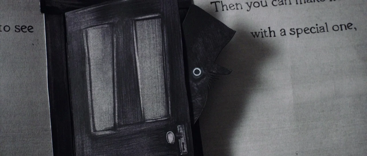 The Babadook (2014) movie still: closeup — A close-up view of a pop-up book page featuring a small black door. A dark paper character peers out from…