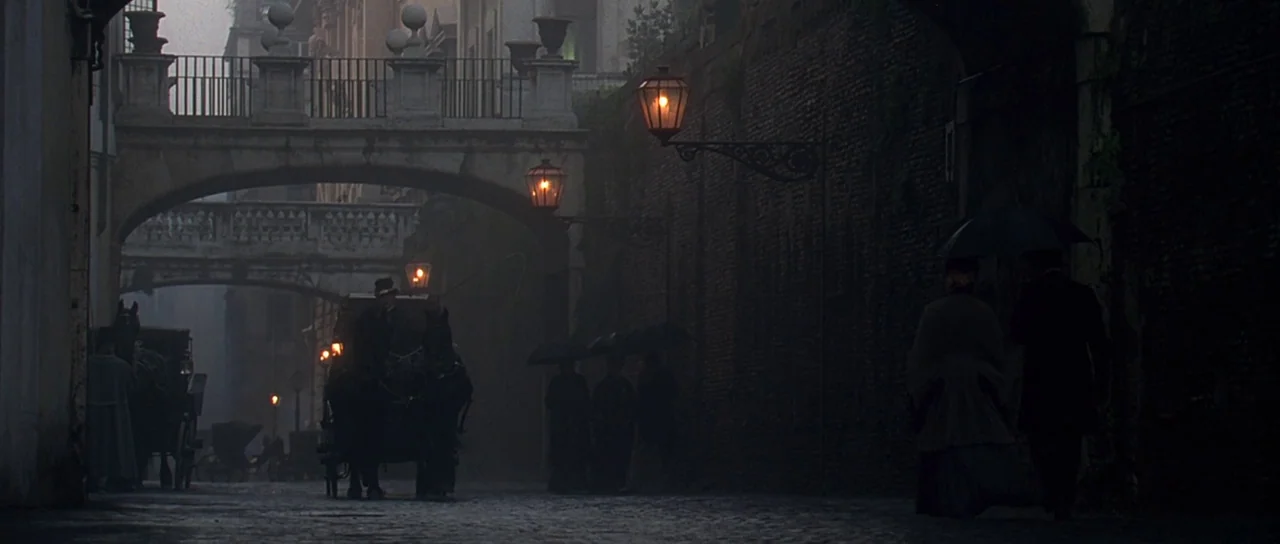 The Portait of a Lady (1996) movie still: wide — A dark, wet cobblestone street is flanked by tall brick walls and stone arches. A horse-drawn…