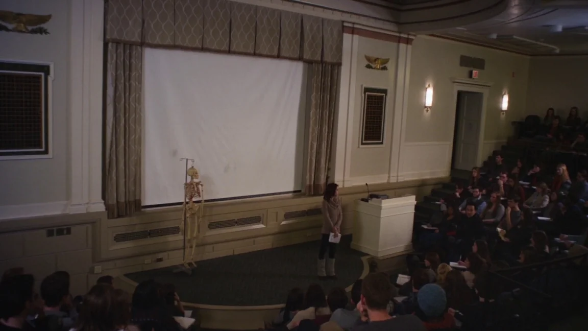 Adult World (2013) movie still: wide — A spacious lecture hall features a large front projection screen and tiered wooden seating. A young woman…