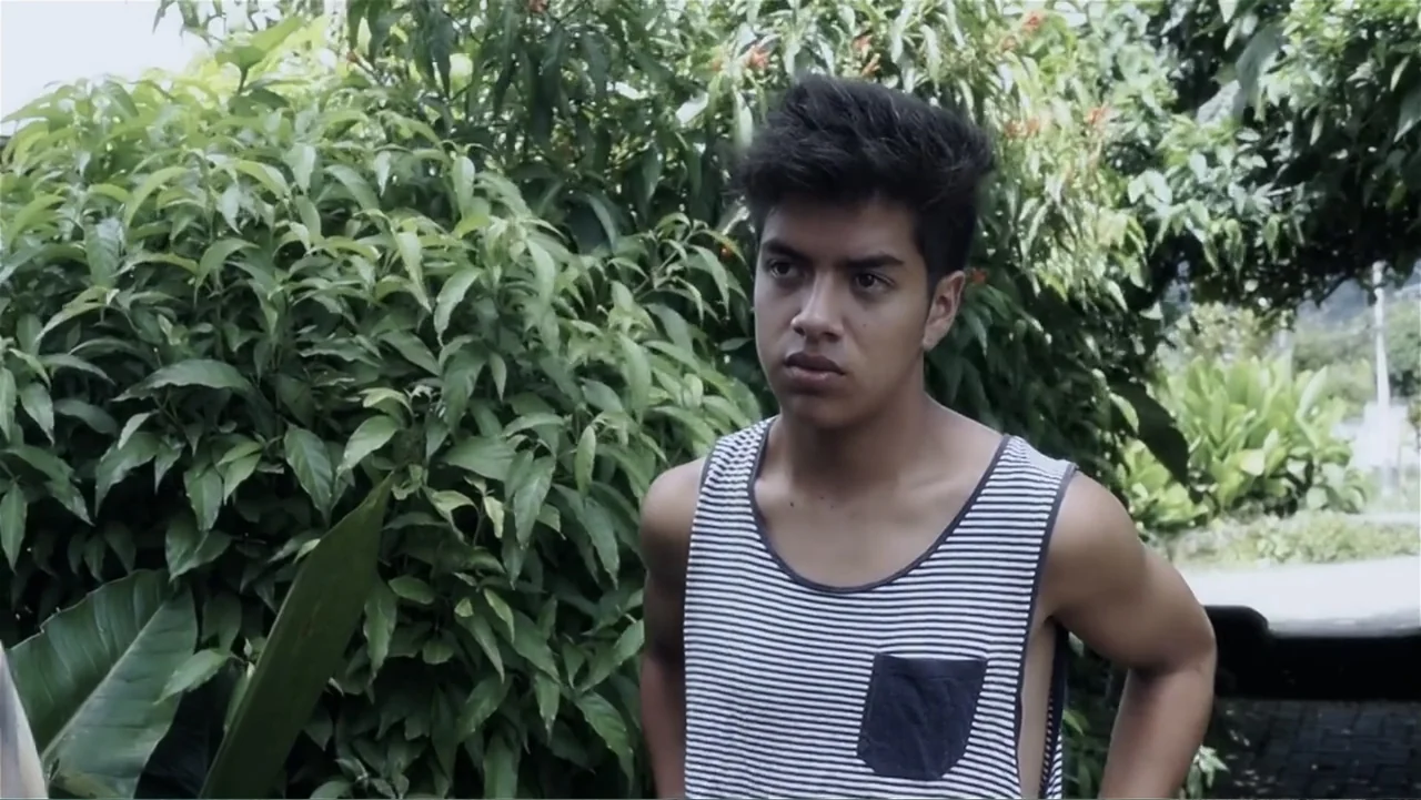 El Duende Sátiro (2016) movie still: medium — A teenage boy stands in front of dense, lush green vegetation outdoors. He looks toward the side while…