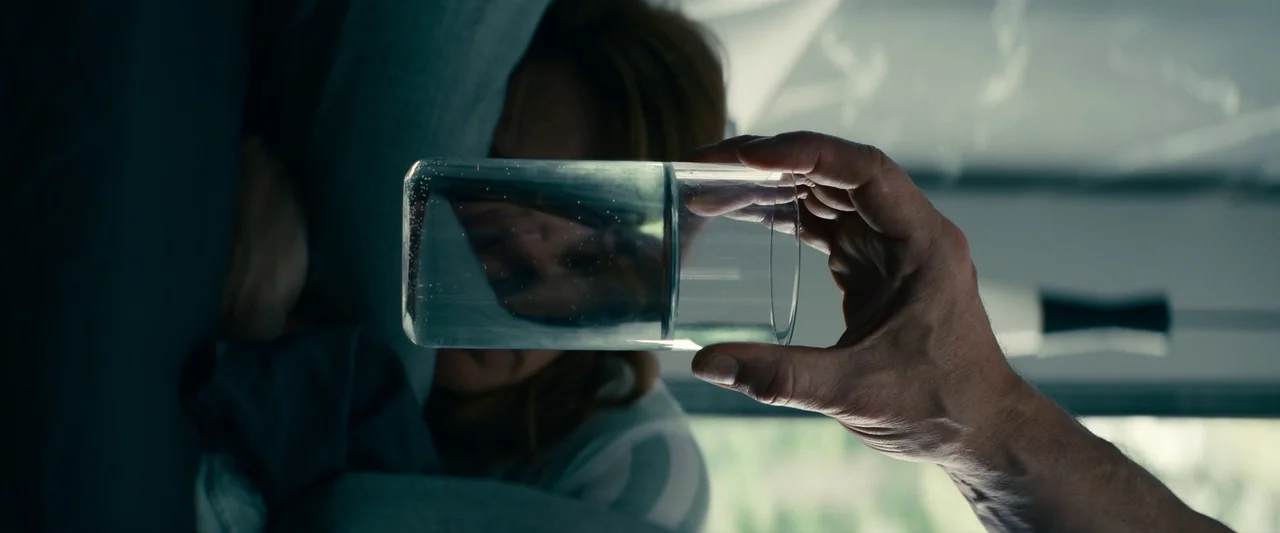 Leave The World Behind (2023) movie still: closeup — A dimly lit room with soft daylight filtering through a window in the background. A man's hand…