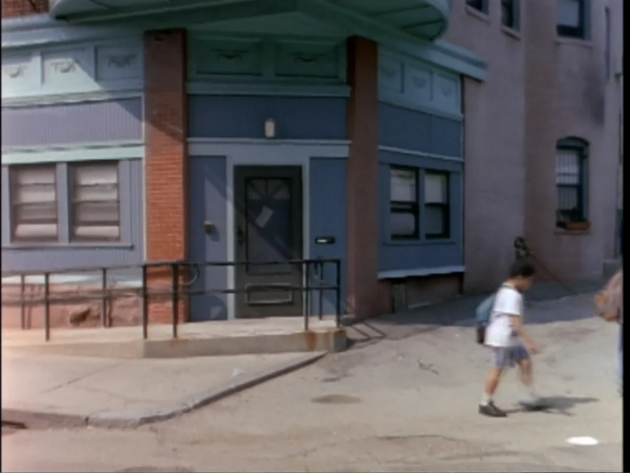5 American Handguns - 5 American Kids (1995) movie still: medium — A corner building features blue painted wood siding and a brick-trimmed entrance.…