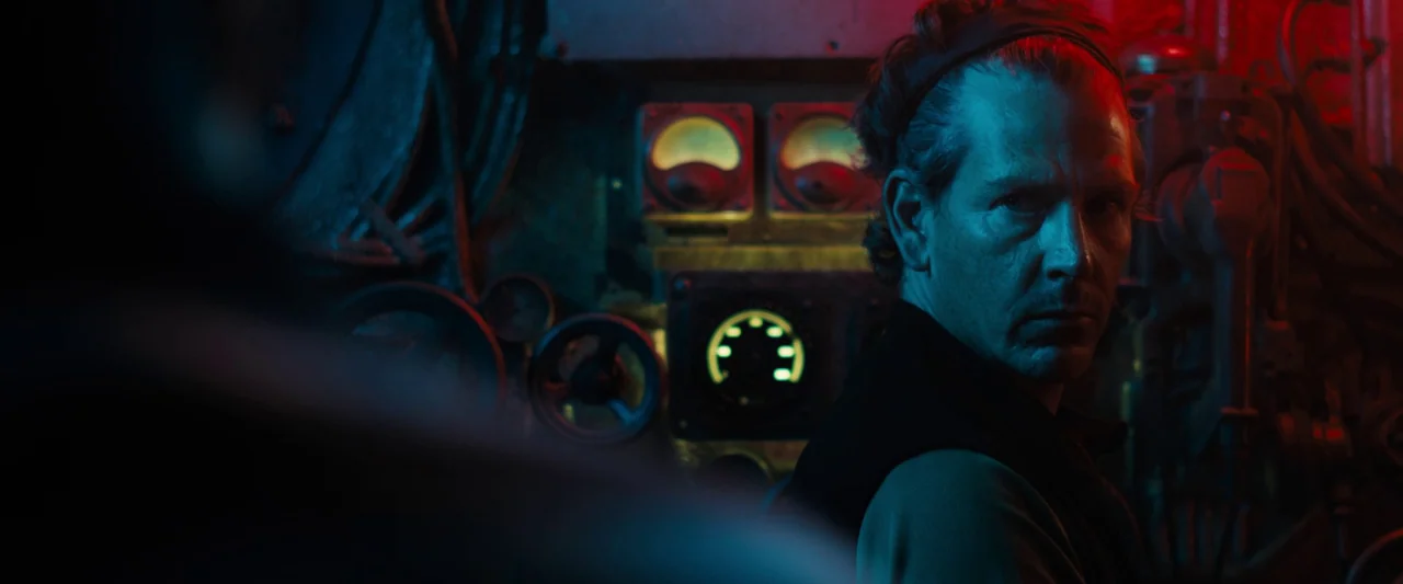 Black Sea (2014) movie still: medium — A cramped and metallic submarine compartment filled with analog gauges and control dials. A man with a…