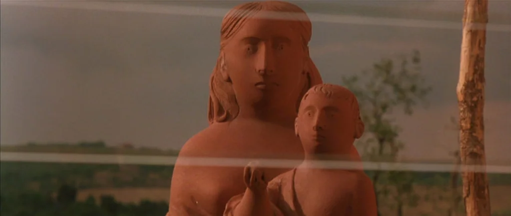 Stealing Beauty (1996) movie still: medium — A terra-cotta sculpture of a woman and child stands in an open field. Horizontal lines from a wire…