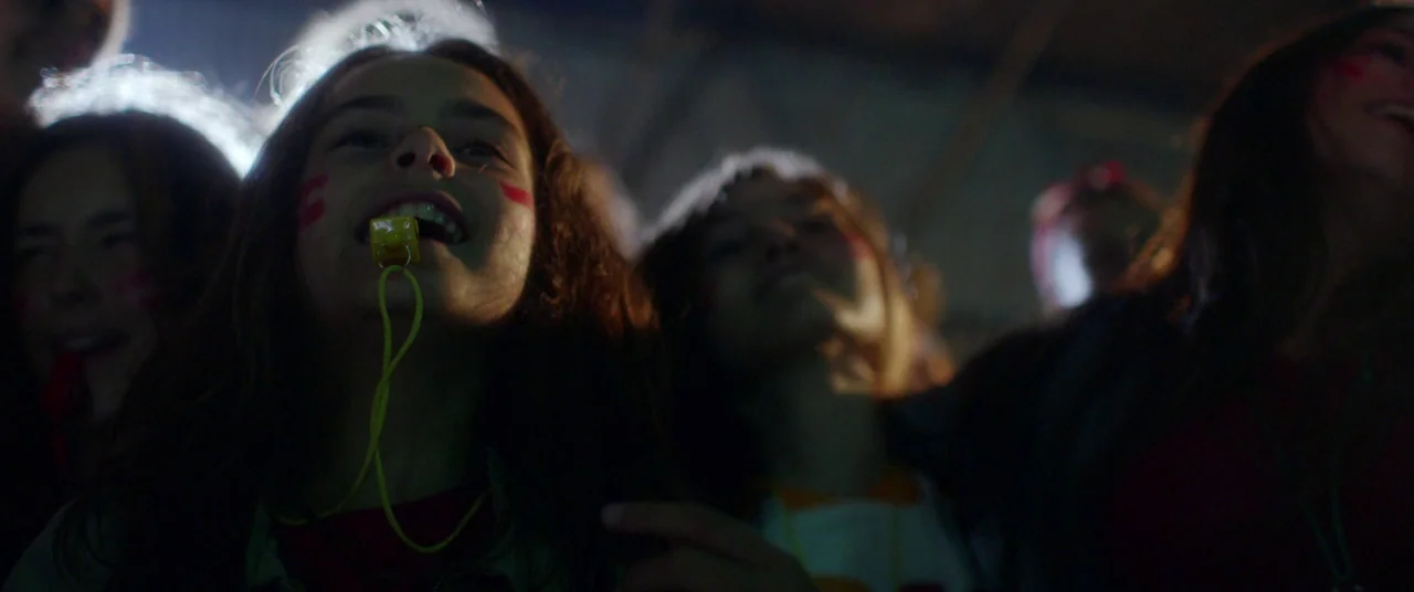 Mustang (2015) movie still: medium — A group of teenagers sits closely together in a dark nighttime setting. The central subject holds a bright…
