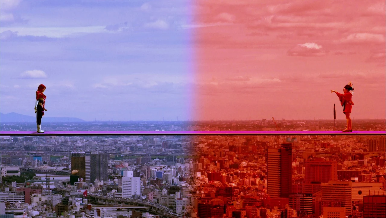 Cutie Honey (2004) movie still: wide — Two individuals stand on a narrow ledge overlooking a vast urban sprawl. The frame is divided by a distinct…