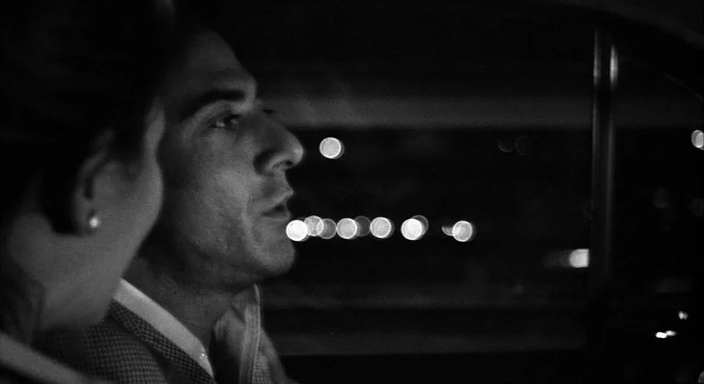 Lenny (1974) movie still: closeup — A man and a woman sit inside a dark vehicle at night. Out-of-focus city lights create a pattern of bokeh circles…