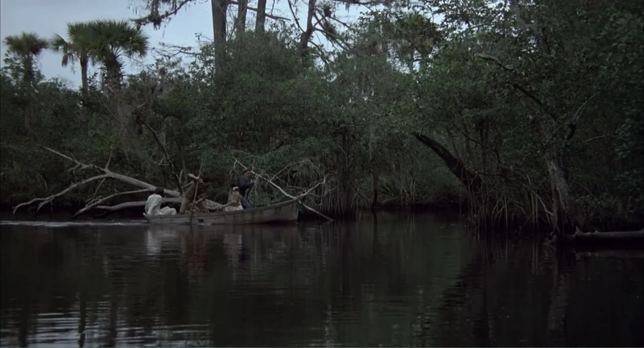 Empire of the Ants (1977) movie still: wide — A murky swamp environment features dense trees, hanging moss, and still dark water. Three people…