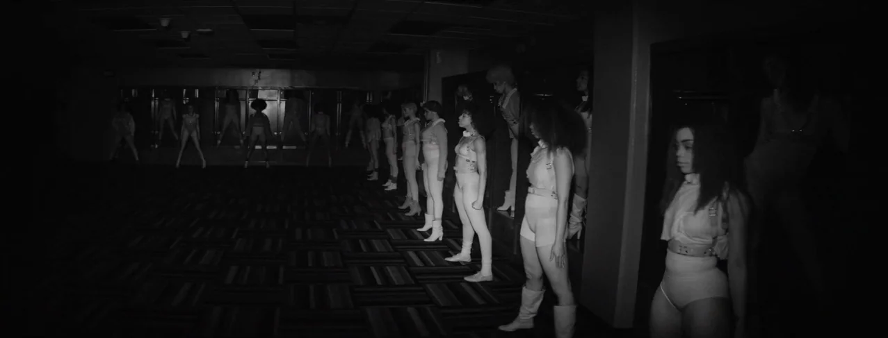Lemonade (2016) movie still: wide — A dimly lit room with rows of storage cabinets lines the dark floor. Many women dressed in white uniforms stand…