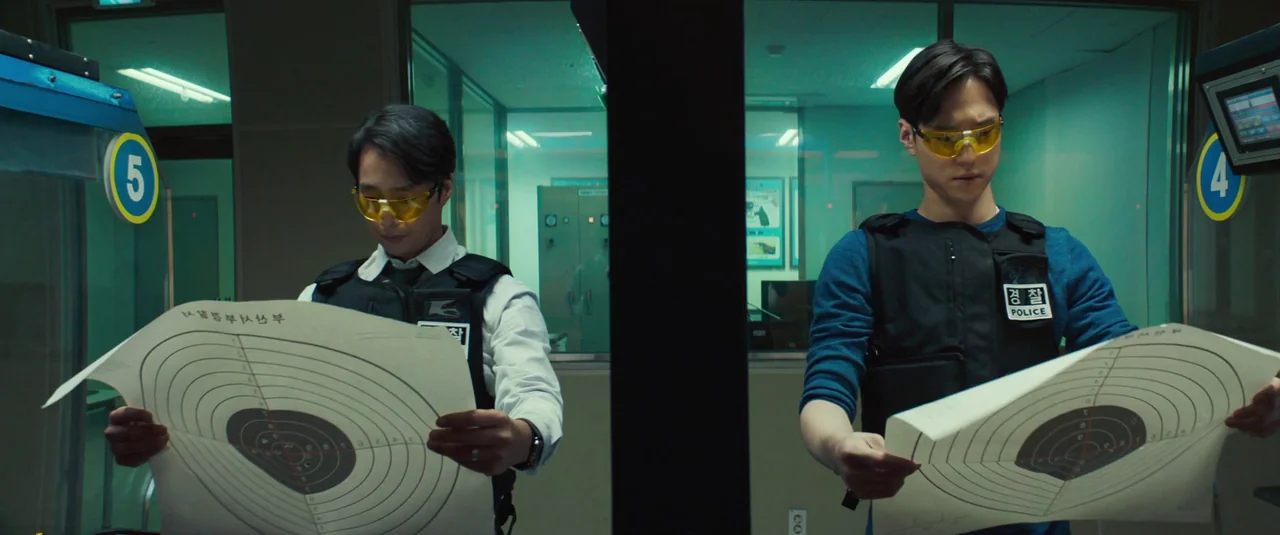 Decision To Leave (2022) movie still: medium — An indoor shooting range features glass partitions between numbered firing lanes. Two police officers…