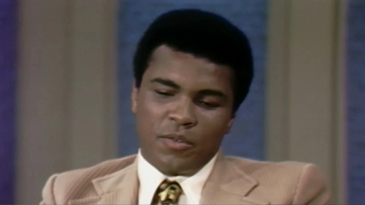Ali & Cavett: The Tale of the Tapes (2018) movie still: closeup — A man in a tan suit sits in a broadcast studio with textured blue walls. He looks…