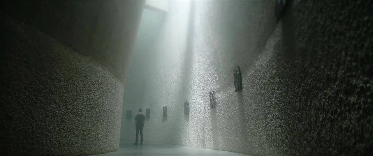 The Divine Fury (2019) movie still: wide — A white, curved-walled room features a series of small vertical frames mounted along surfaces. A lone…