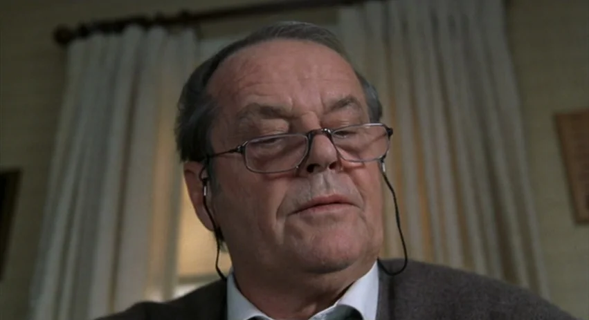 About Schmidt movie still: closeup — A residential interior features a person standing before sheer white curtains on a window. The subject wears…