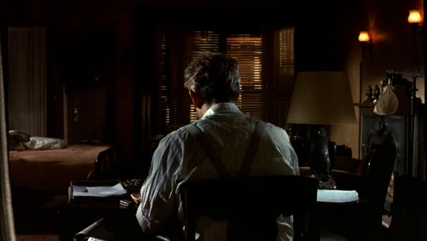 Hammett (1982) movie still: medium — A dark study with wood paneled walls and warm glowing lamps in the evening. A man sits at a desk with his back…