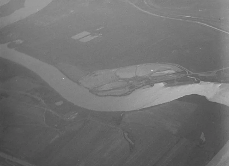 Wings (1966) movie still: establishing — An aerial view shows a meandering river carving through flat agricultural fields. A long, thin island sits…