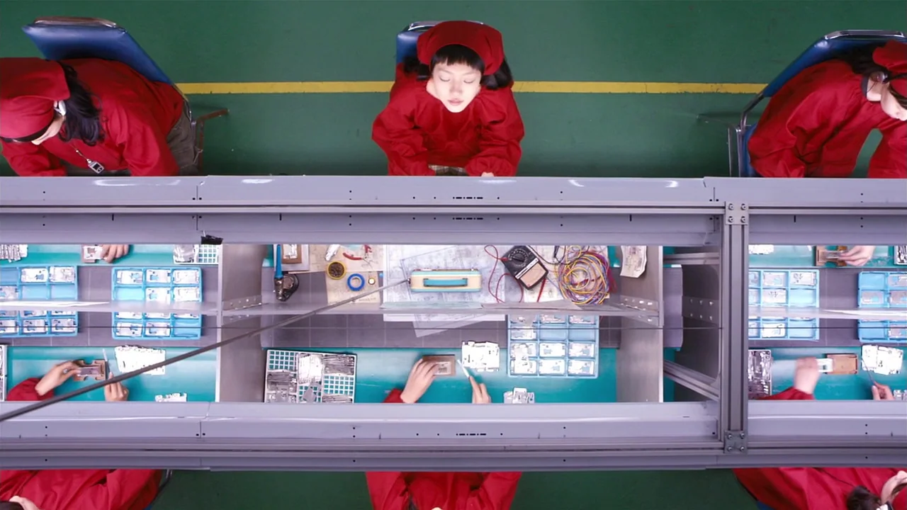 I’m A Cyborg, But That’s Okay (2006) movie still: wide — A top-down view of a brightly lit industrial assembly line with uniform green flooring.…