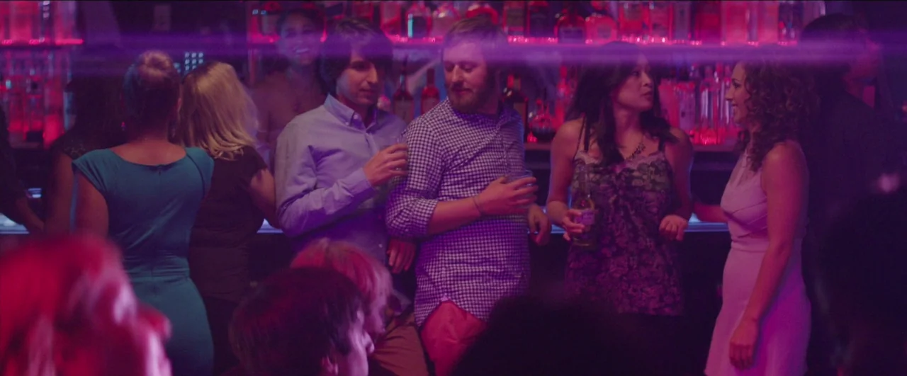 Dean (2016) movie still: medium — A crowded bar interior features a backlit counter with shelves of colorful alcohol bottles. A diverse group of…