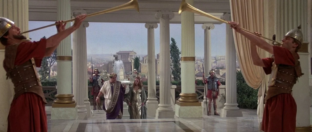 History of the World: Part 1 (1981) movie still: wide — An ornate Roman-style colonnade overlooks a city with a central fountain. Two…