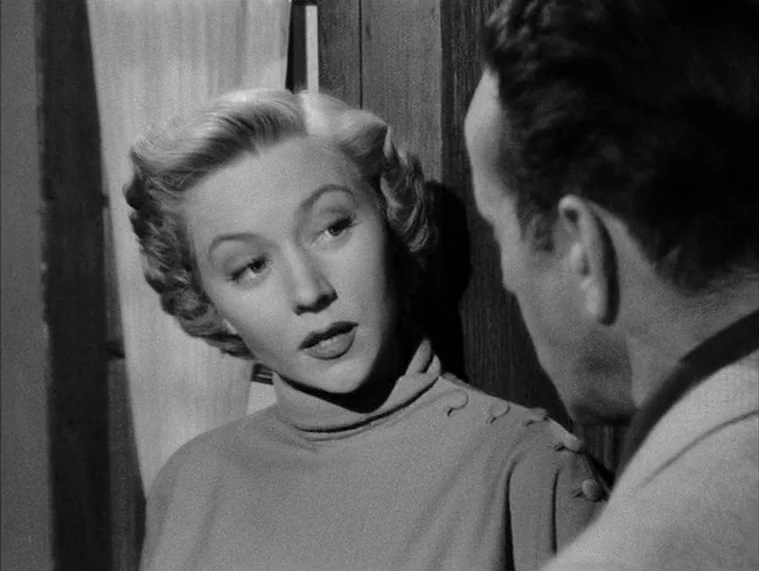 In a Lonely Place (1950) movie still: closeup — An interior space features a woman looking at a man during a conversation. The woman stands slightly…