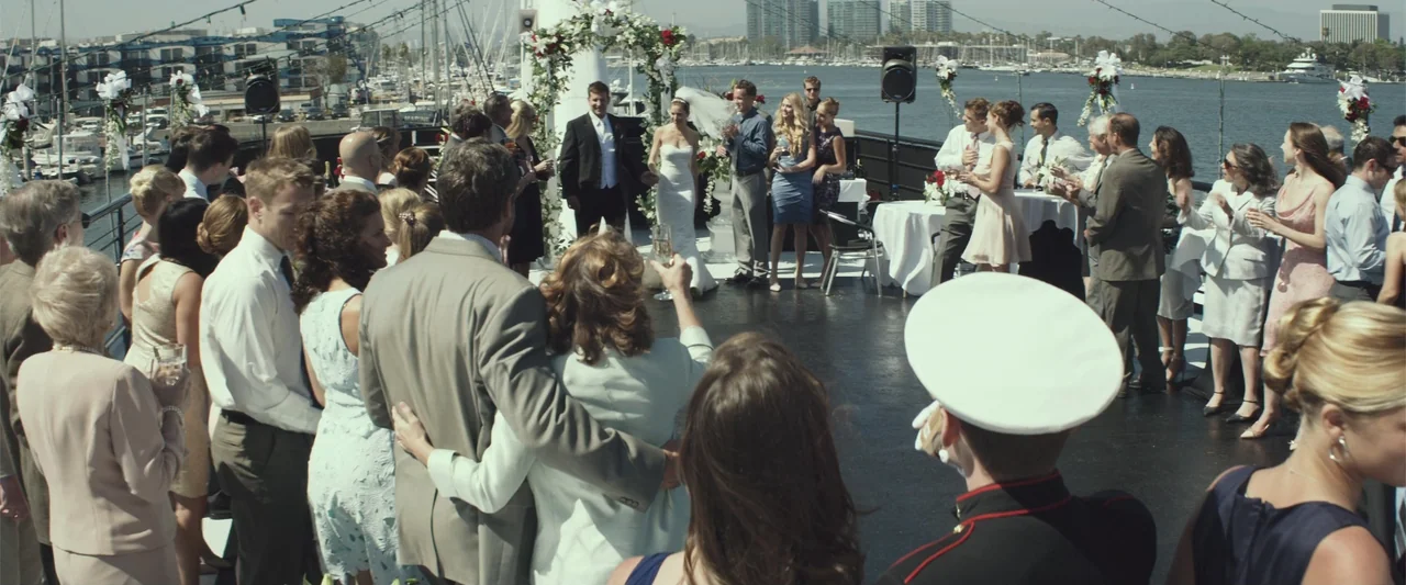 American Sniper (2014) movie still: wide — A group of guests gathers on the deck of a boat docked at a marina. A bride and groom stand under a…