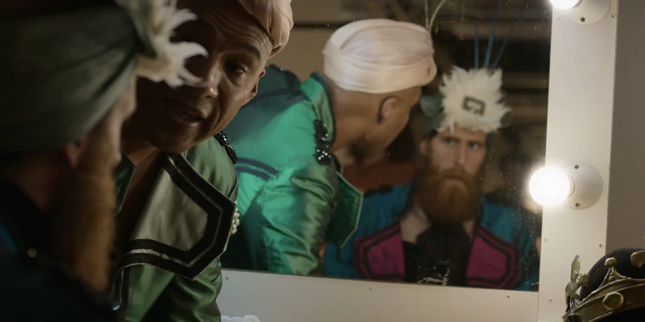 The Three Wise Men: The Truth (2022) movie still: medium — Two men in elaborate stage costumes stand before a bright vanity mirror. The reflection…