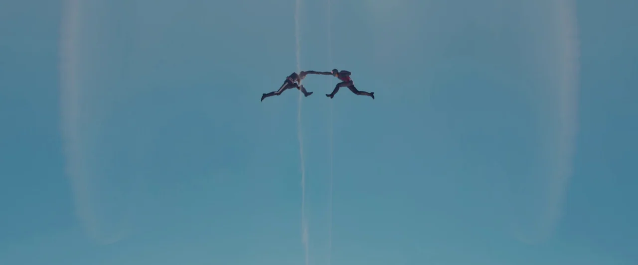 Shin Kamen Rider (2023) movie still: wide — A vast, clear blue sky serves as the backdrop for two falling skydivers. The two figures are positioned…
