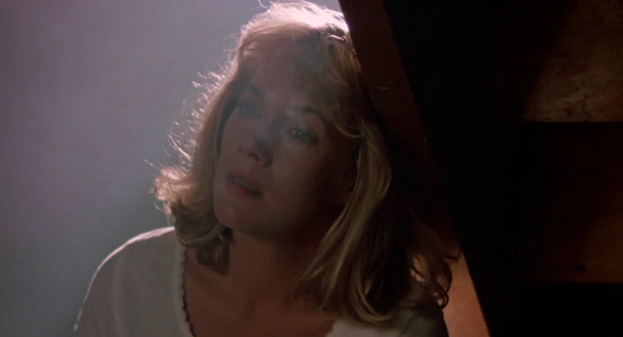 Peggy Sue Got Married (1986) movie still: closeup — A dimly lit indoor setting with visible wooden structural elements of a staircase. A blonde…
