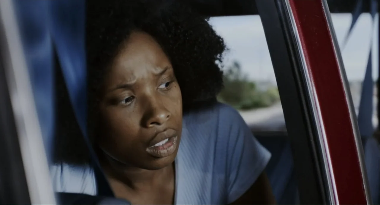 Elles (2018) movie still: closeup — A close view inside a car cabin shows a woman looking toward the window. The car frame and blue curtain are…