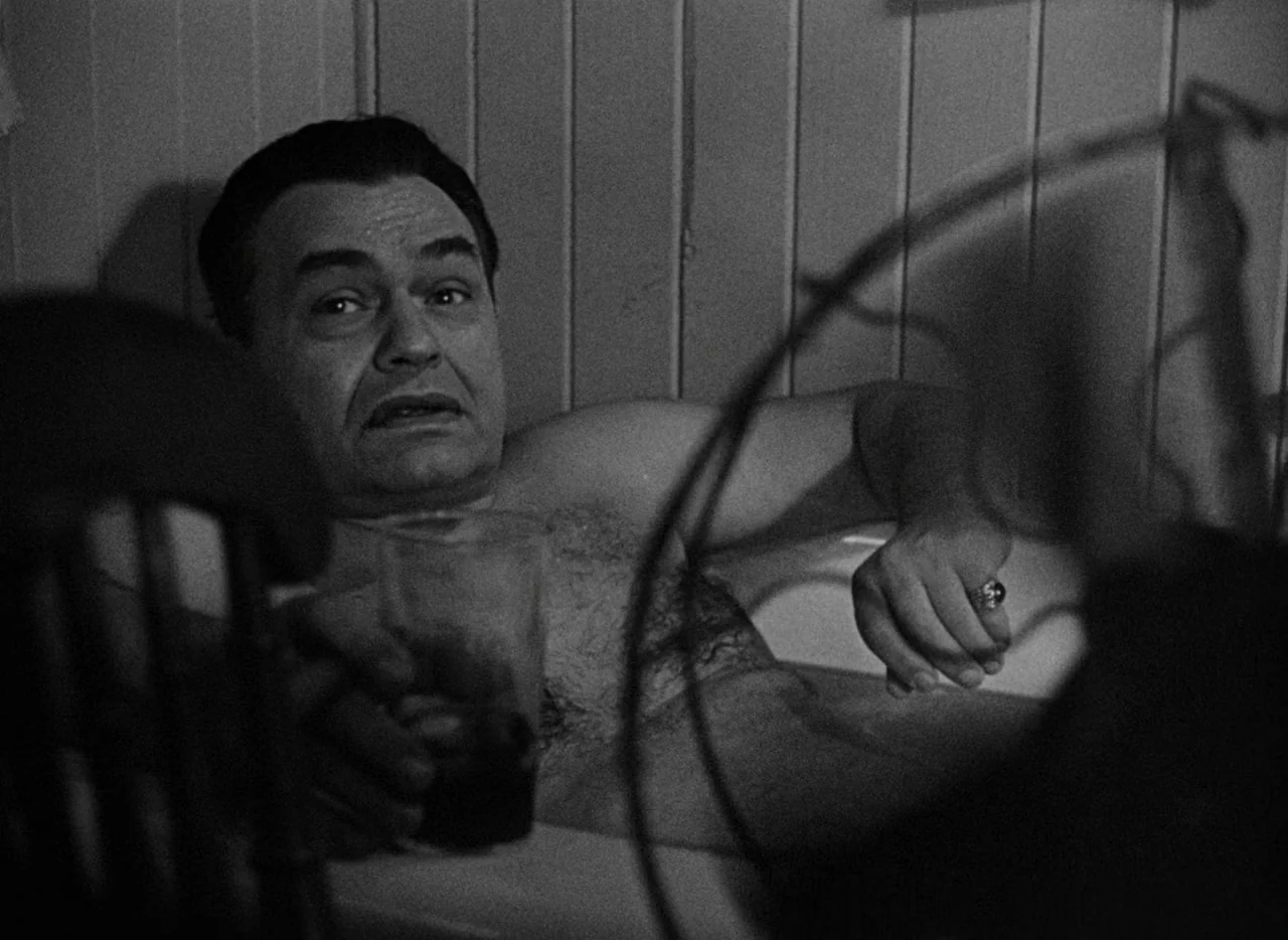 Key Largo (1948) movie still: medium — A man lies in a bathtub against a wall with vertically paneled wood. He holds a glass while looking forward…