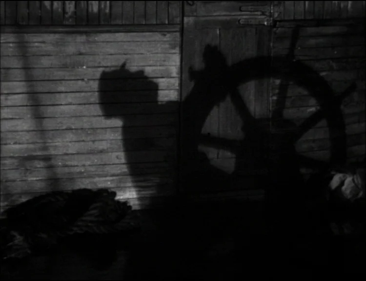Dracula (1931) movie still: medium — Horizontal wooden planks form a wall on a ship deck at night. A dark shadow of a person stands next to the…