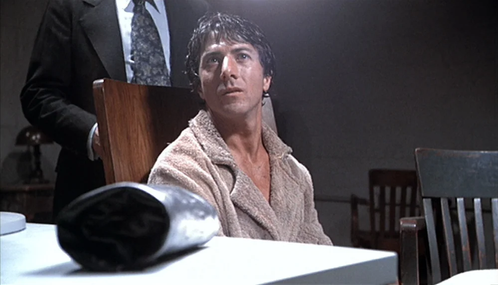 Marathon Man (1976) movie still: medium — A dimly lit room contains wooden furniture and a white table. A man in a bathrobe sits at the table, while…