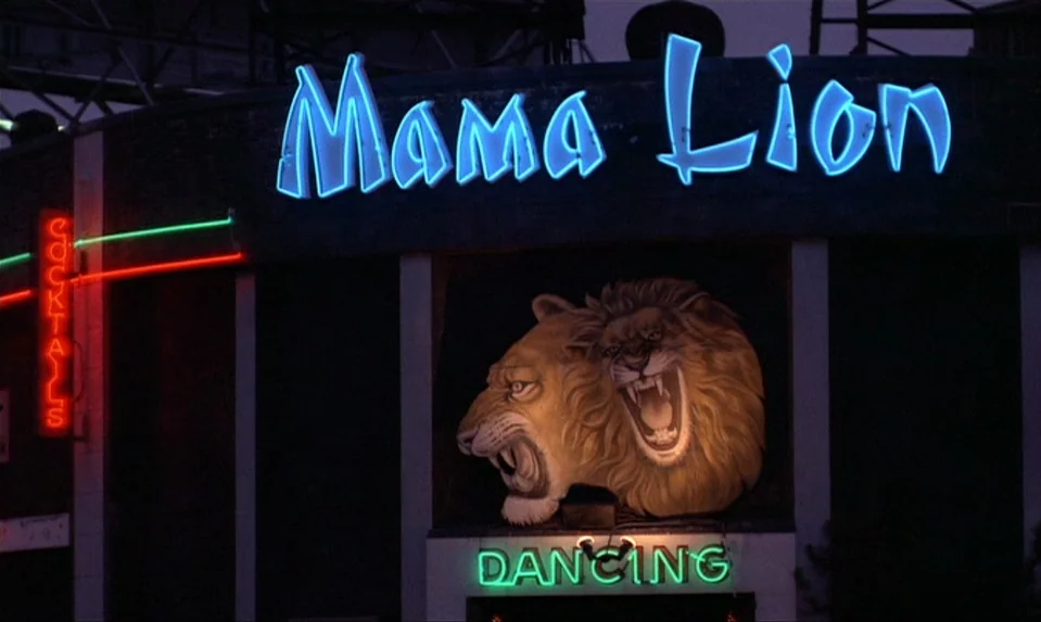 Lions Love (1969) movie still: establishing — The exterior of a nightclub building features a prominent blue neon sign reading Mama Lion. A large…
