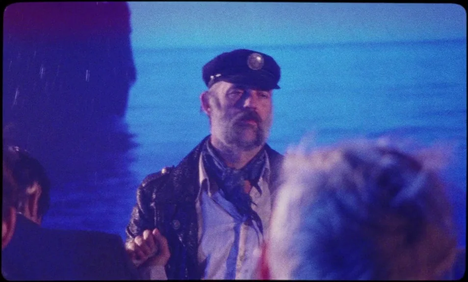 The Wild Boys (2017) movie still: medium — A man stands near water at night under artificial blue light. A dark structure looms on the left side…