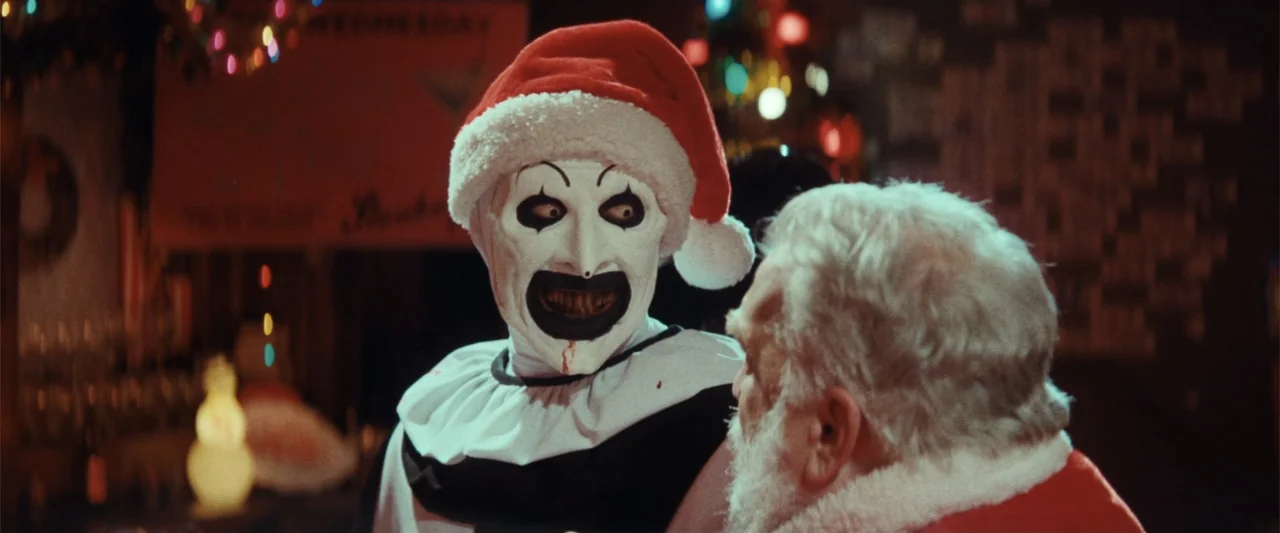 Terrifier 3 (2024) movie still: medium — A dark interior space features holiday decorations in the background with multicolored bokeh lights. A…