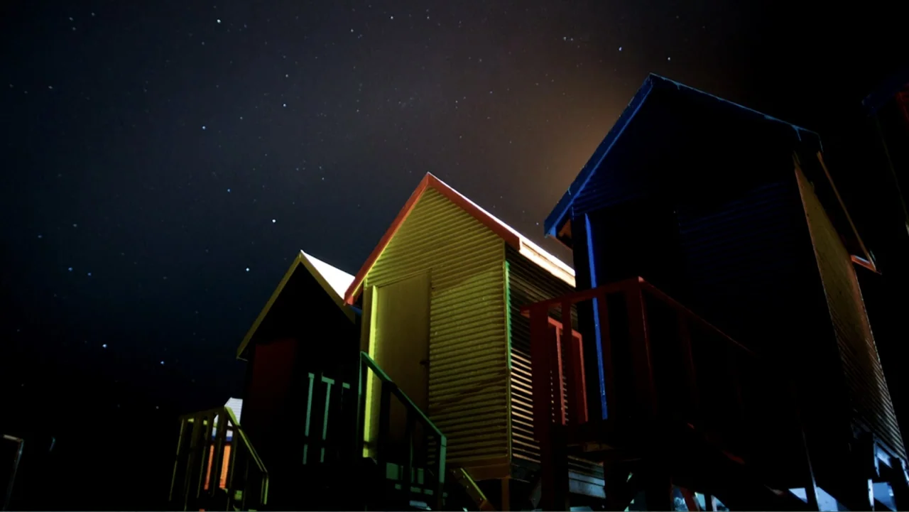 Air Jaws: Night Stalker (2016) movie still: wide — Three colorful wooden beach huts stand on stilts under a dark starry night sky. The structures…