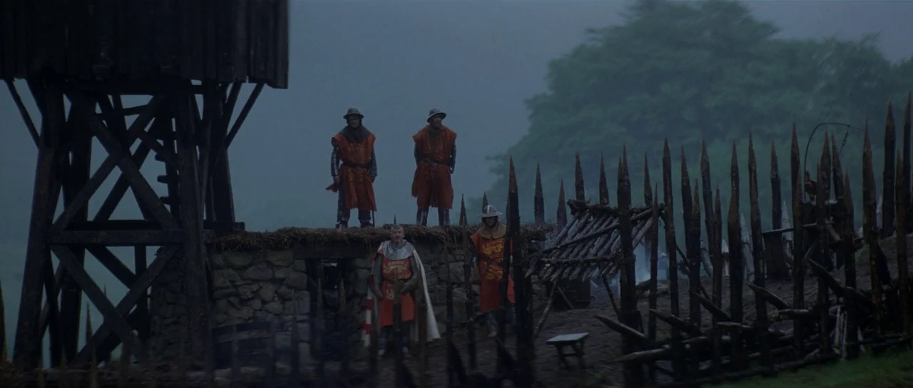 Braveheart (1995) movie still: wide — A stone fortification with a tall wooden watchtower stands under a gray overcast sky. Four soldiers in…