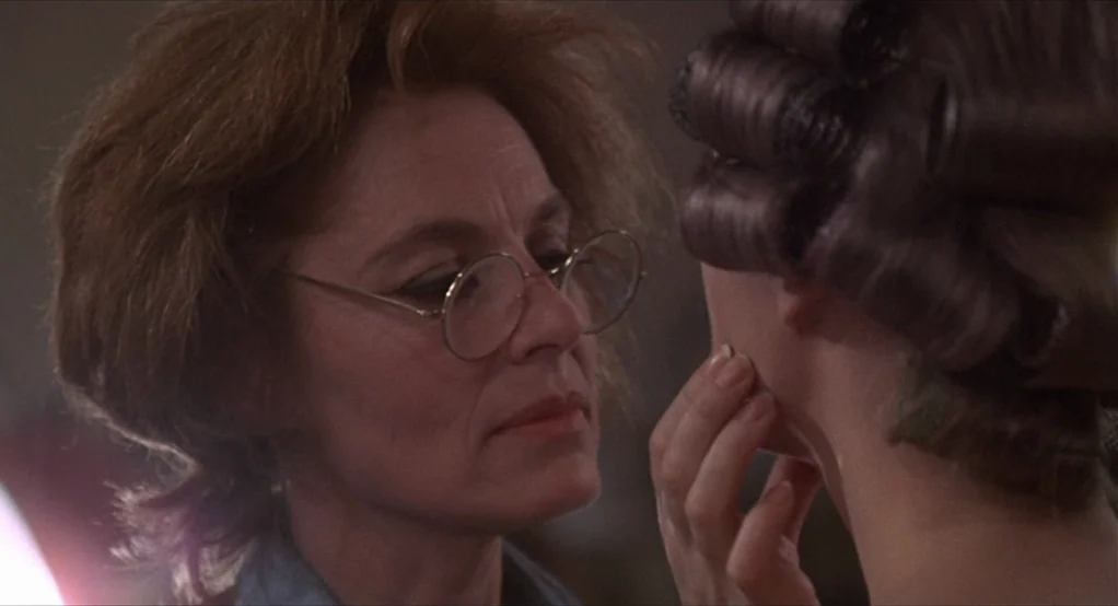 Puzzle of a Downfall Child (1970) movie still: closeup — A close-up shot of two women near a mirror during a beauty routine. An older woman with…