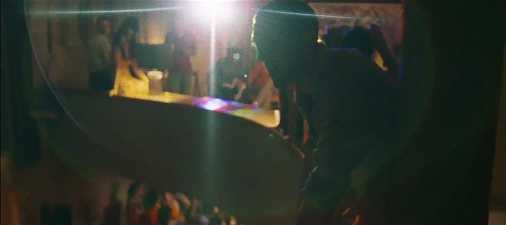 Irréversible (2002) movie still: medium — A crowded, dimly lit nightclub bar features a central bright light source. A silhouetted figure stands in…