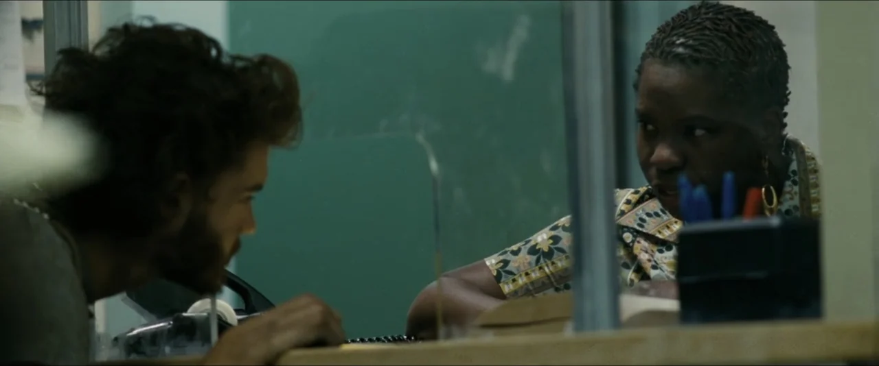 Into the Wild (2007) movie still: medium — An administrative counter features a green wall and a clear plexiglass partition screen. A man stands at…