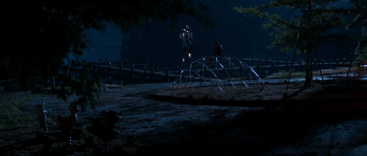 Spider Man: Homecoming (2017) movie still: wide — A night landscape features a dark waterfront with a wooden pier and playground equipment. A…