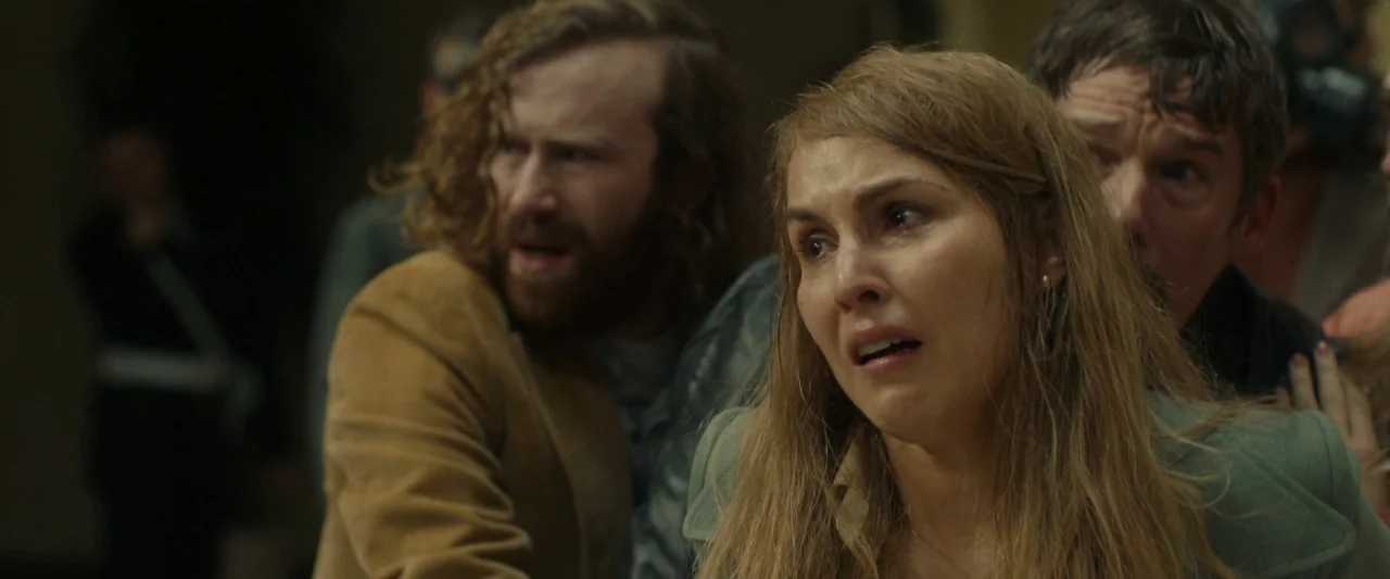 Stockholm (2019) movie still: medium — A dimly lit indoor corridor with multiple people standing close together in a group. The individuals exhibit…