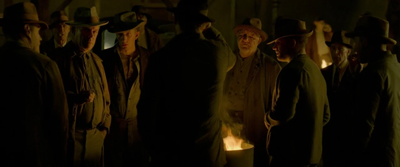 Lawless (2012) movie still: medium — A group of men wearing fedoras stand gathered in a circle at night. They are warming their hands over a fire…