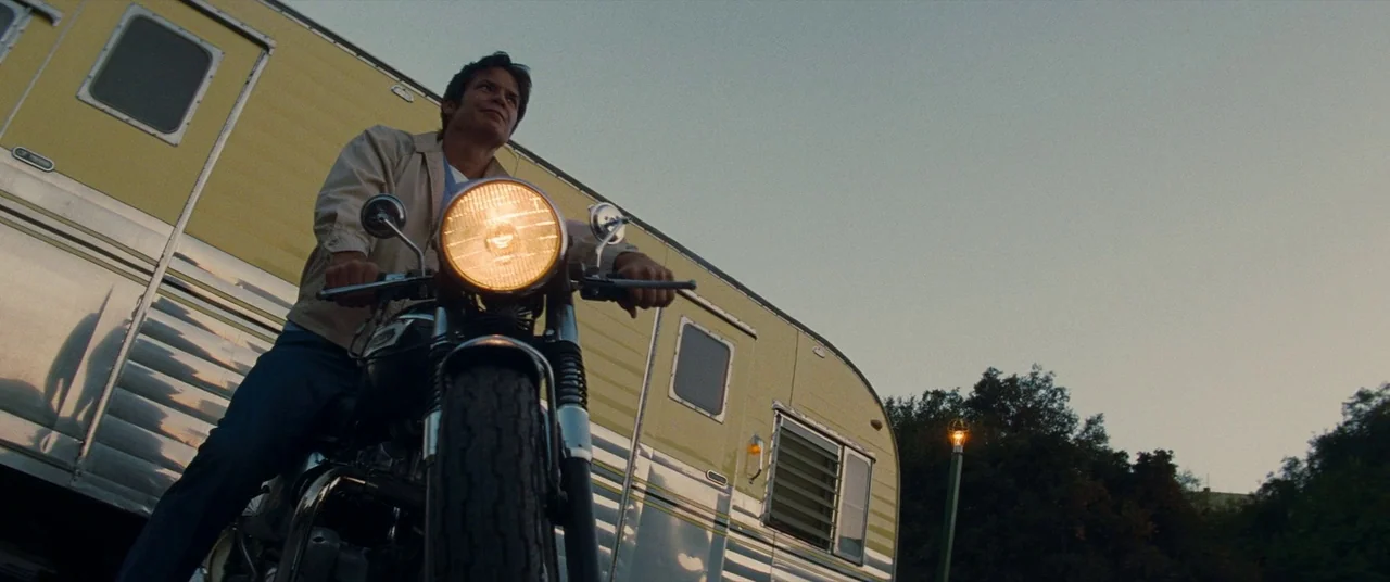 Once Upon a Time… In Hollywood (2019) movie still: medium — A man sits on a vintage motorcycle parked in front of a yellow metal trailer. The…