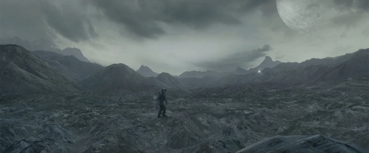 DISTANT (2026) movie still: wide — A vast, barren rocky landscape spans the horizon under a cloudy, grey sky. A lone astronaut in a dark suit stands…