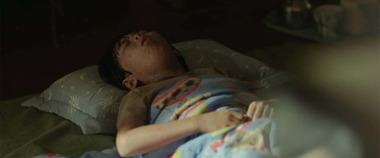 Along with the Gods: The Last 49 Days (2018) movie still: medium — A dimly lit room contains a bed with a child covered by a blanket. The child lies…