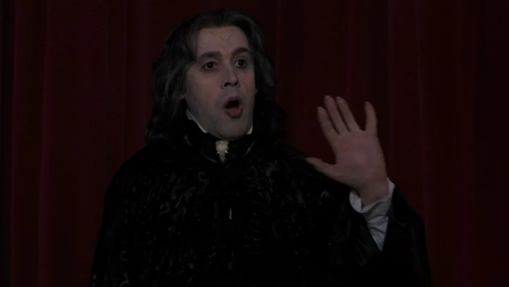 Interview With The Vampire movie still: medium — A dark, velvet-curtained space provides the backdrop for a central figure in costume. The…